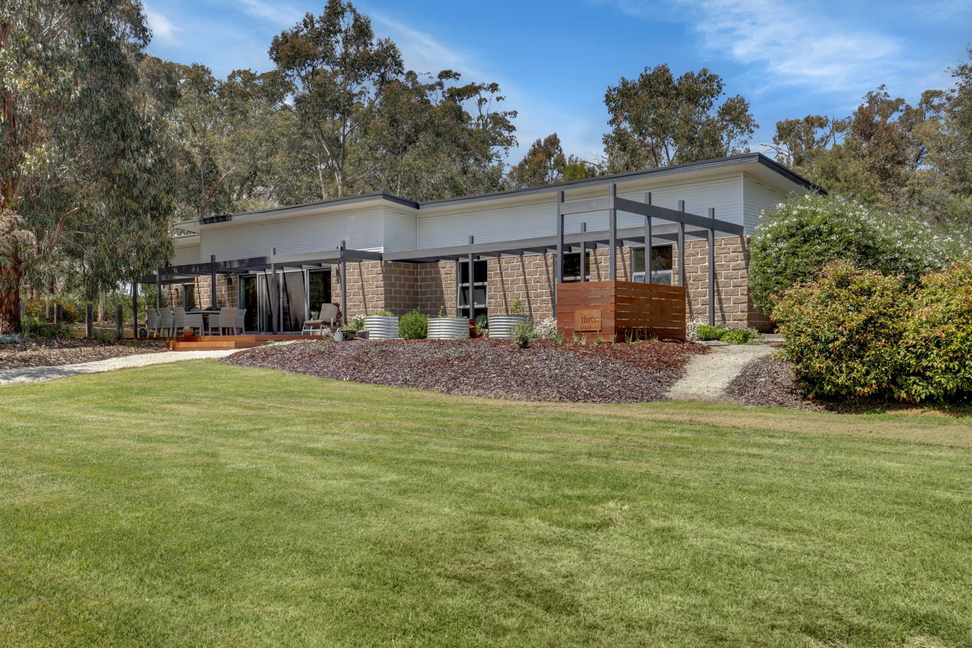 Modern single-story house with stone and gray exterior, wooden deck, and large green lawn in front