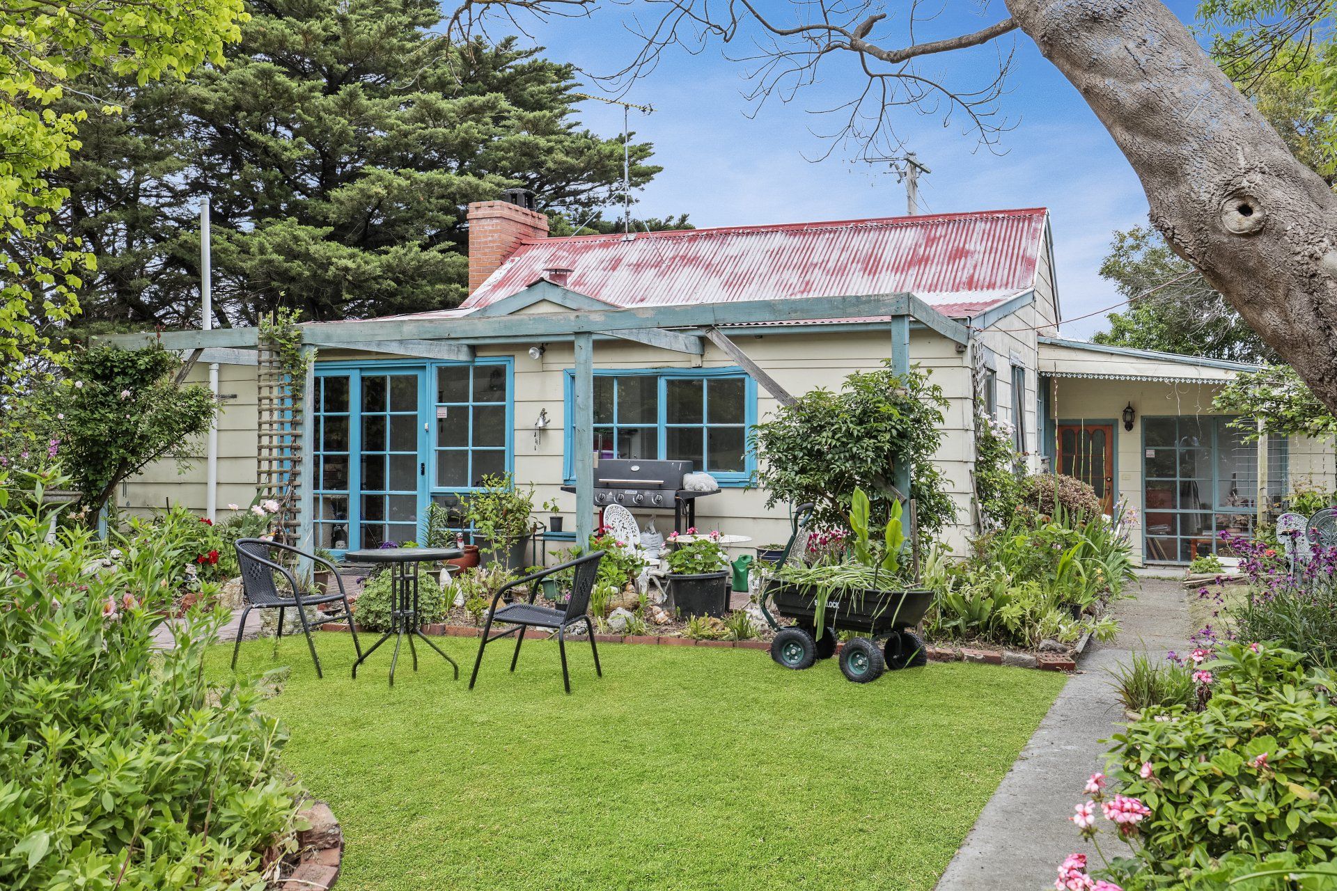 Charming white cottage with blue trim, red roof, and a lush garden lawn under a clear sky.