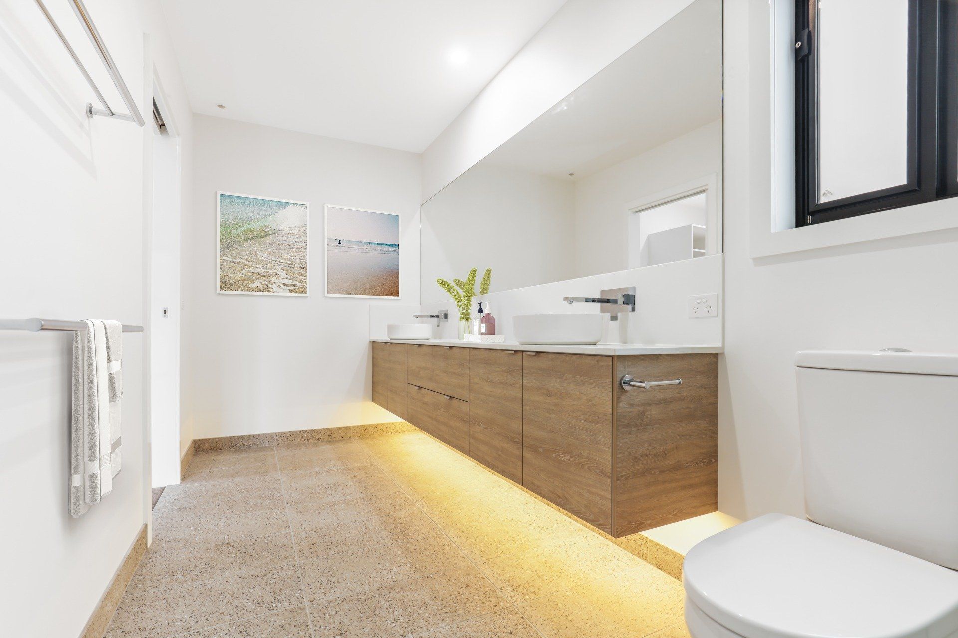Modern white bathroom with wood vanity, wall mirror, and warm under-cabinet lighting