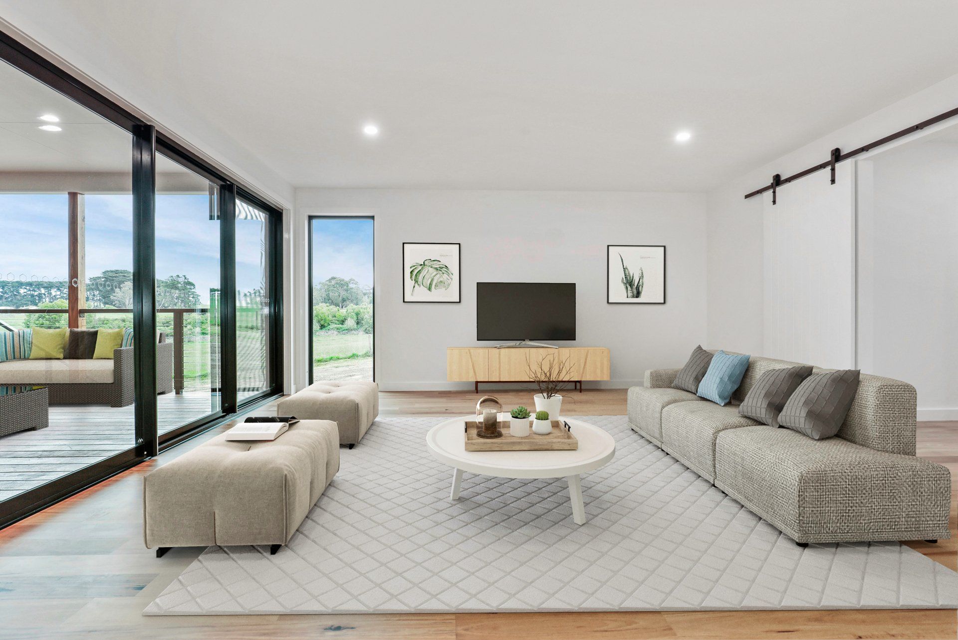 Modern living room with gray sectional, ottoman, TV, large sliding doors, and bright minimalist decor.