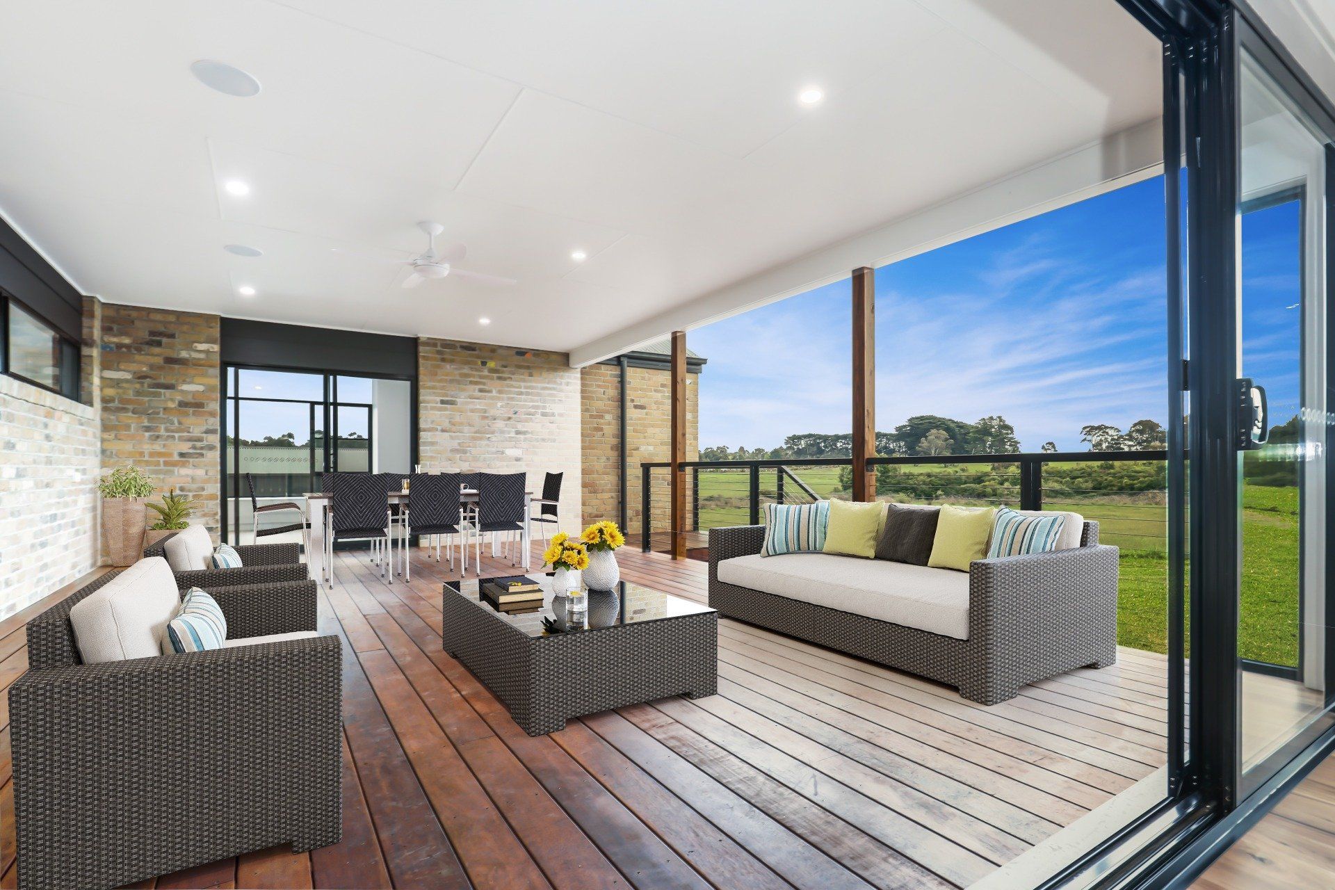 Covered patio with wicker seating, coffee table, and a grassy backyard view through open glass doors
