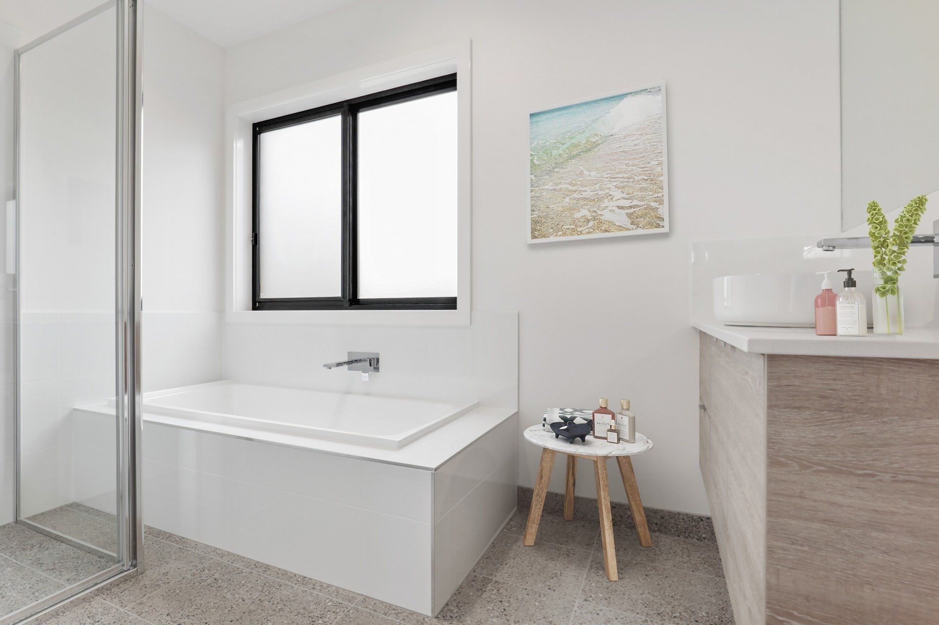 Bright modern bathroom with a bathtub, window, vanity, and small stool, in white and wood tones