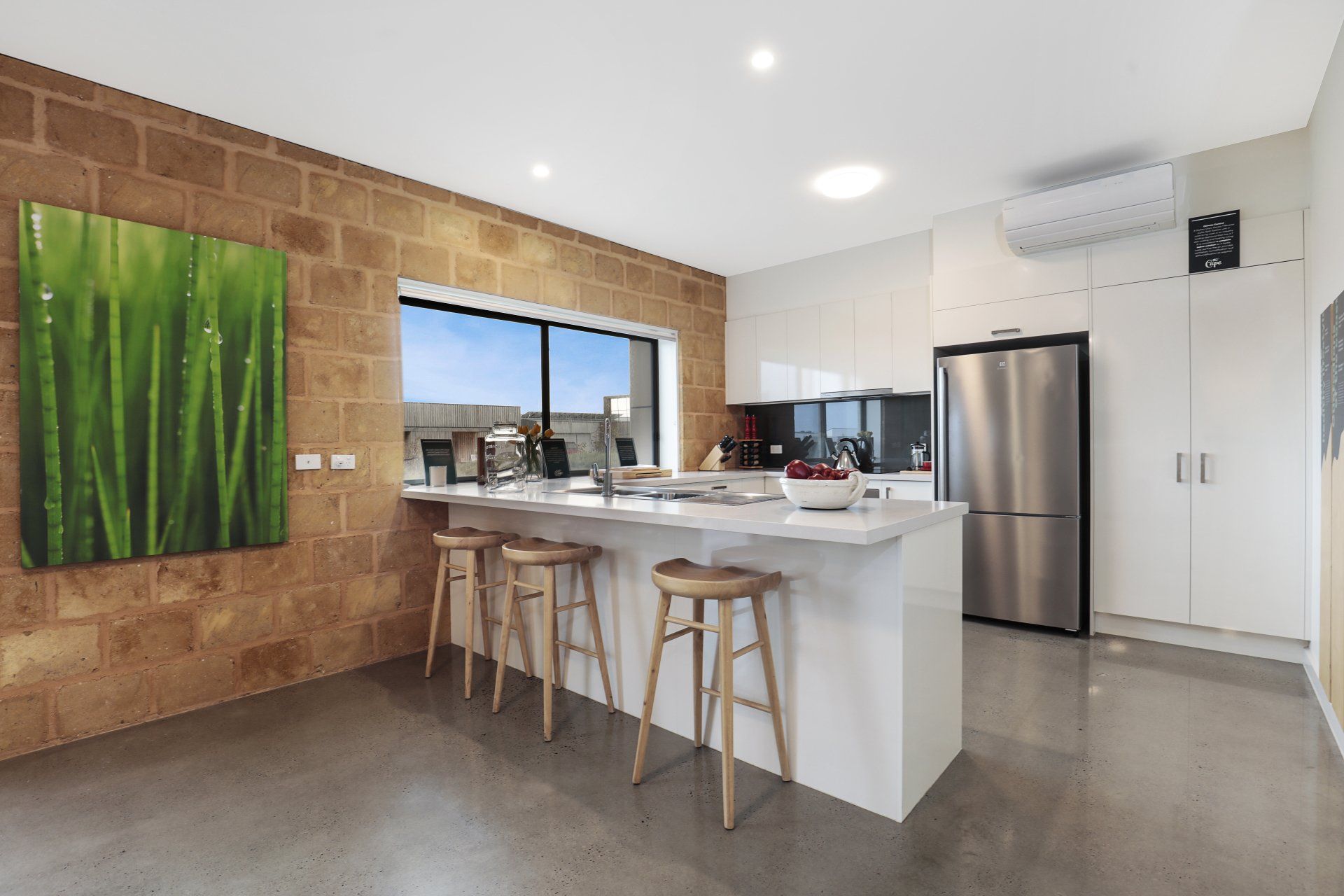 Modern kitchen with island, bar stools, stainless steel fridge, and a large window overlooking the water.