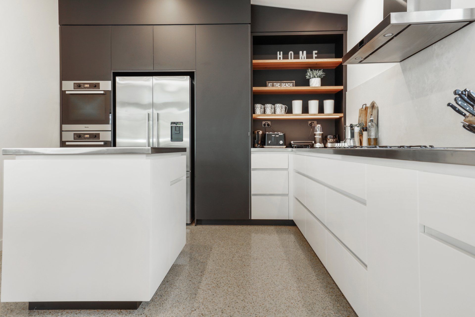 Modern minimalist kitchen with white cabinets, dark wood shelves, and stainless steel appliances