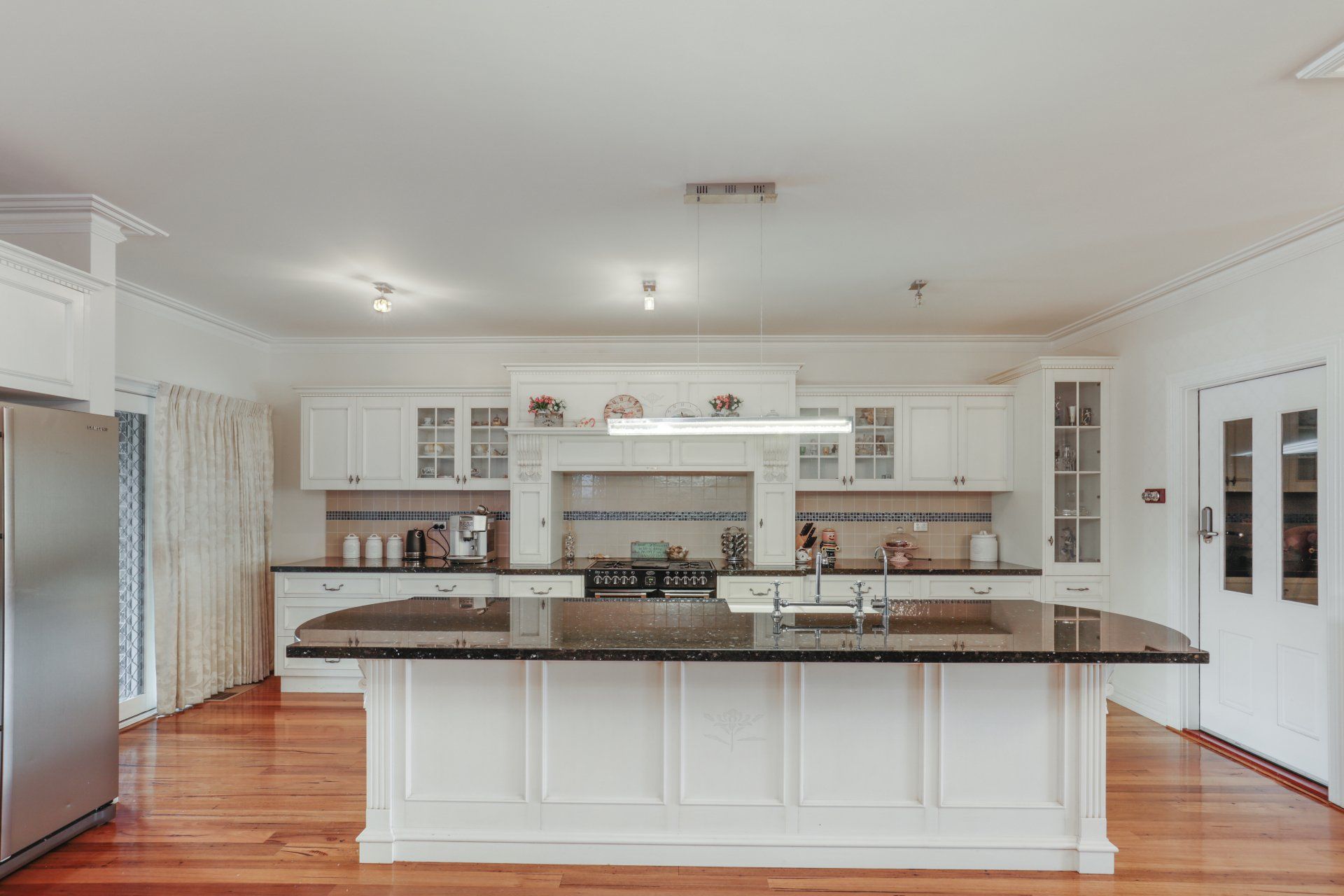 Bright white kitchen with central island, dark granite countertops, hardwood floors, and stainless appliances