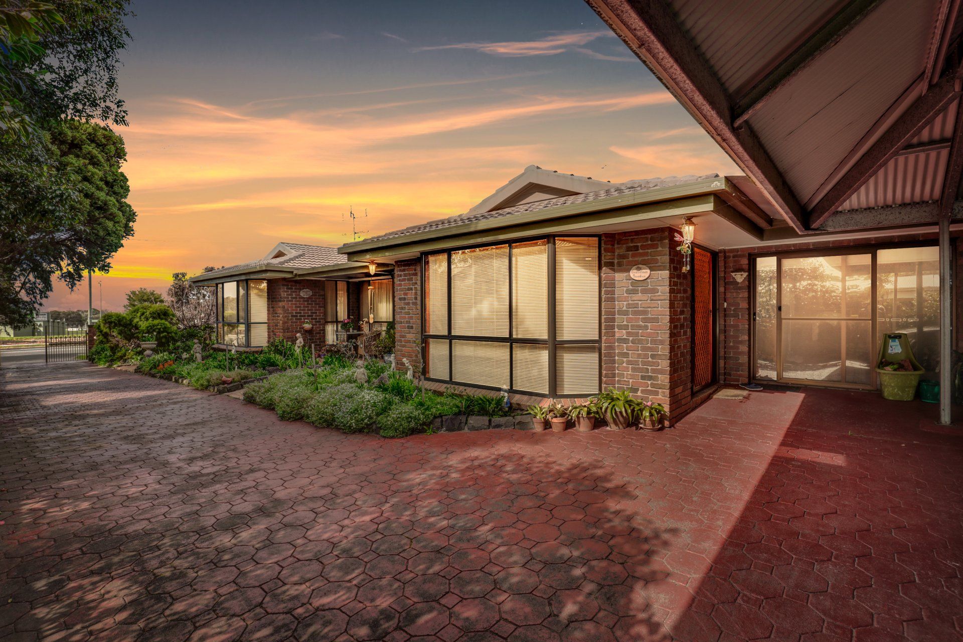 Brick home exterior at sunset with a wide driveway, front porch, and landscaped garden.