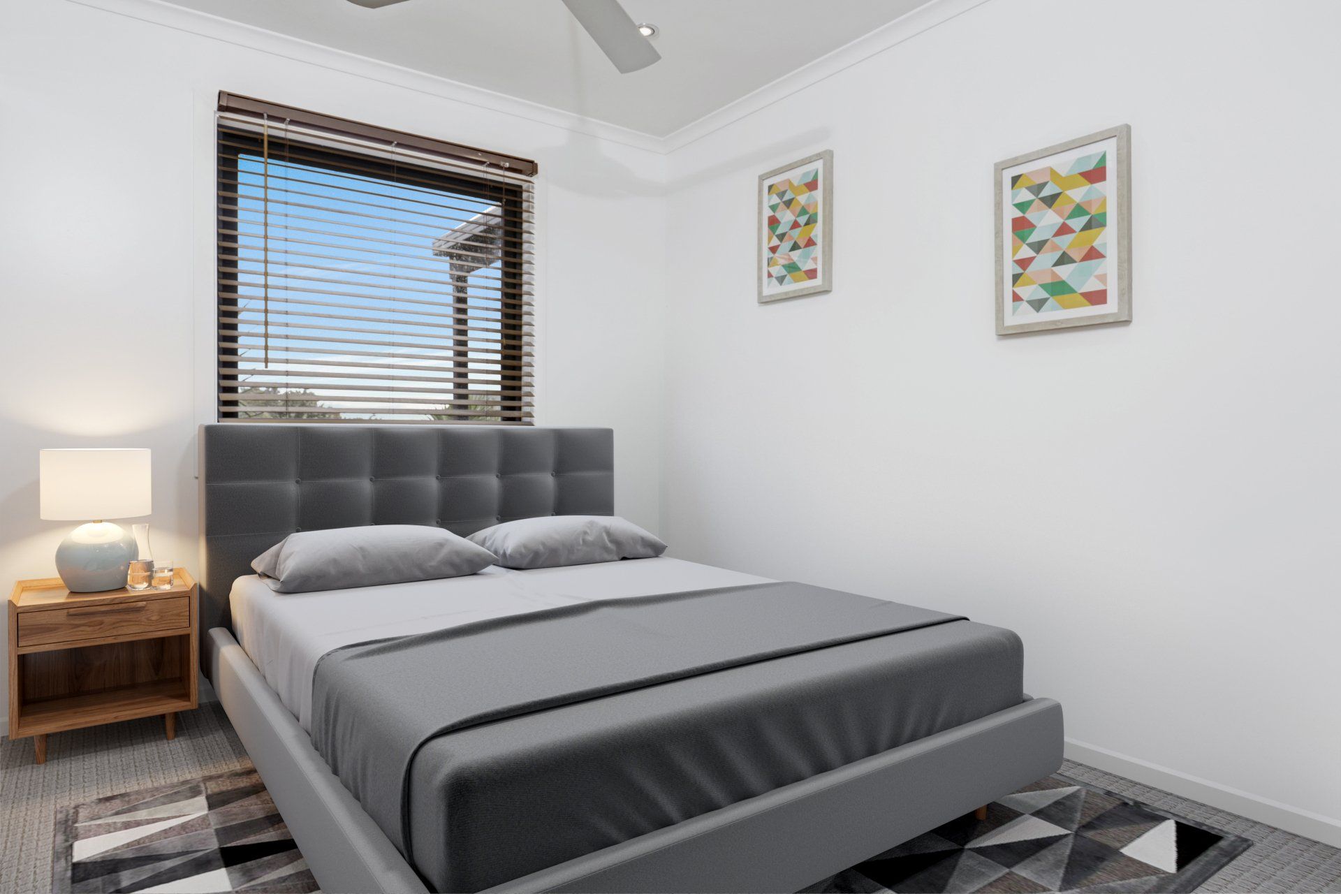 Bright modern bedroom with a gray bed, bedside lamp, window blinds, and framed wall art.