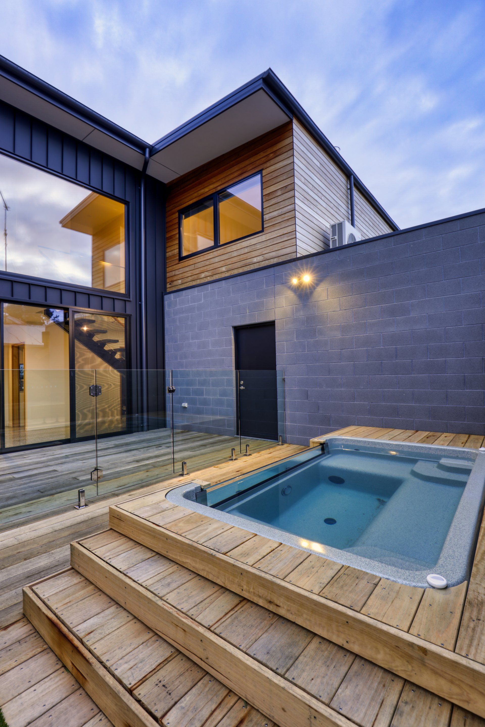 Modern house patio with a small blue hot tub beside a dark brick wall at dusk