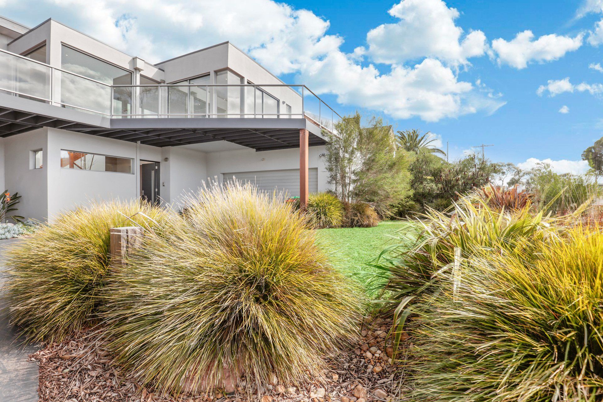 Modern house with balcony, native landscaping, and green lawn under a blue sky