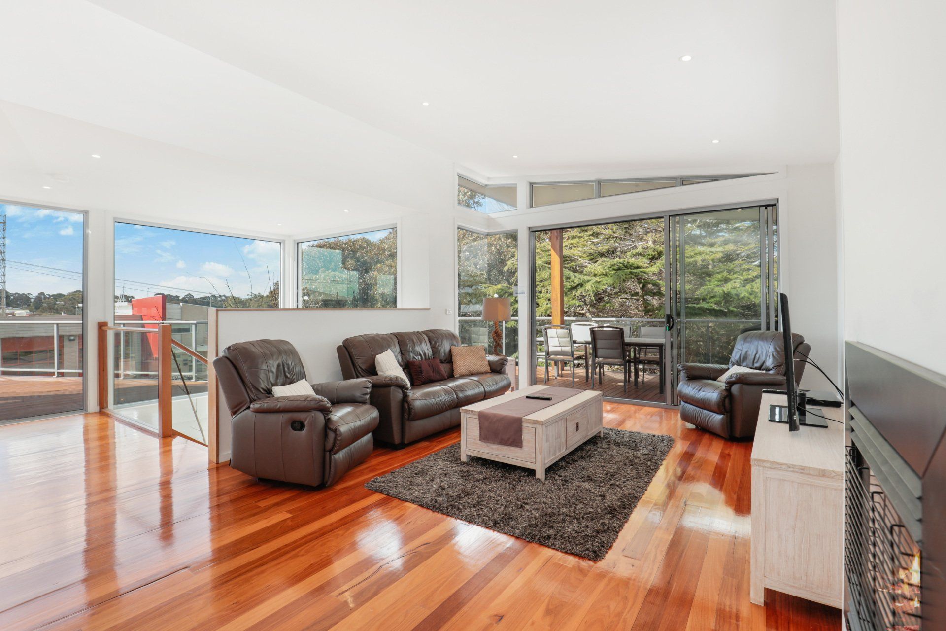 Bright modern living room with hardwood floors, brown sofa, black chair, rug, and floor-to-ceiling windows