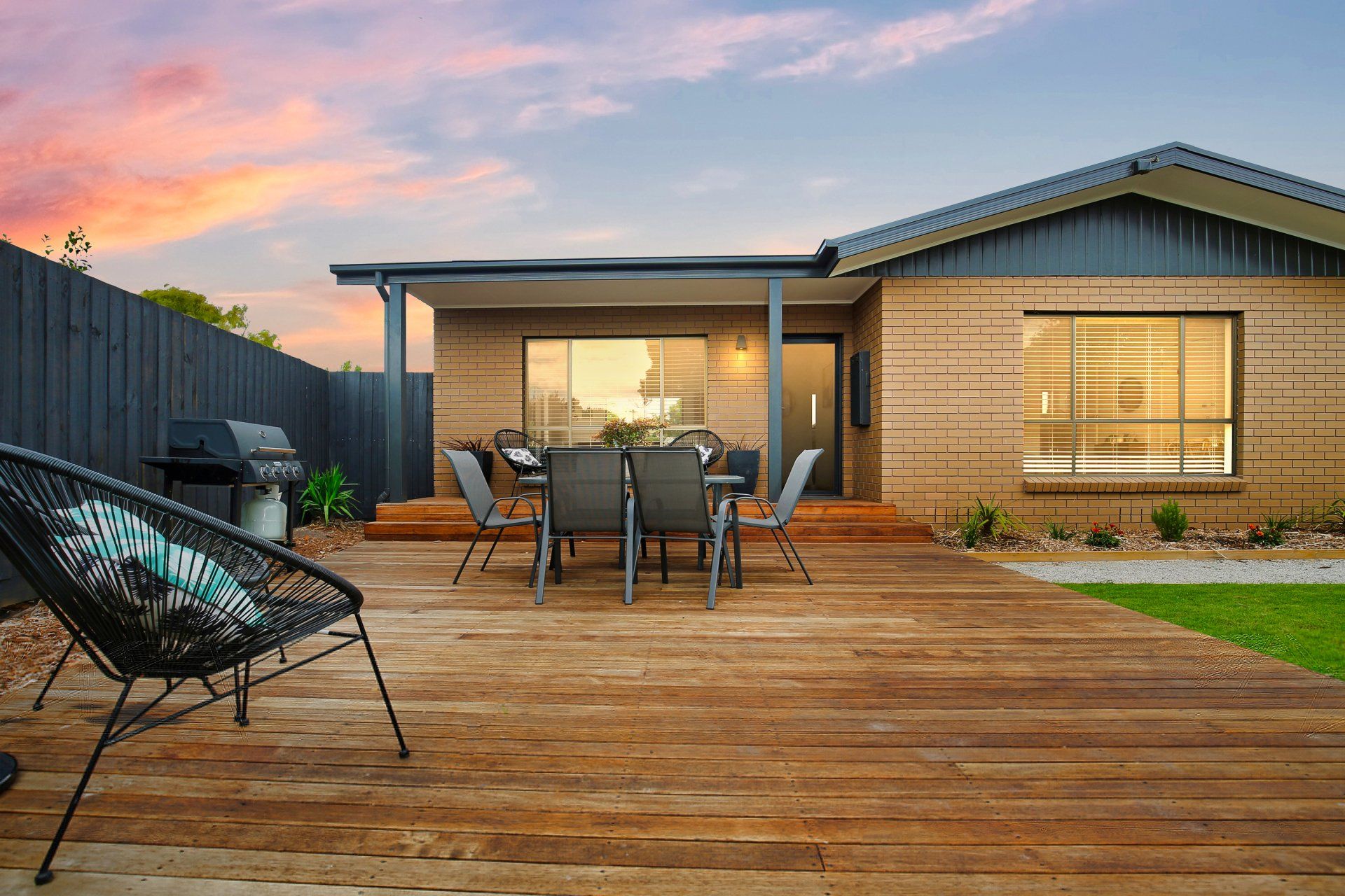 Backyard deck with outdoor dining table and chairs beside a modern house at sunset
