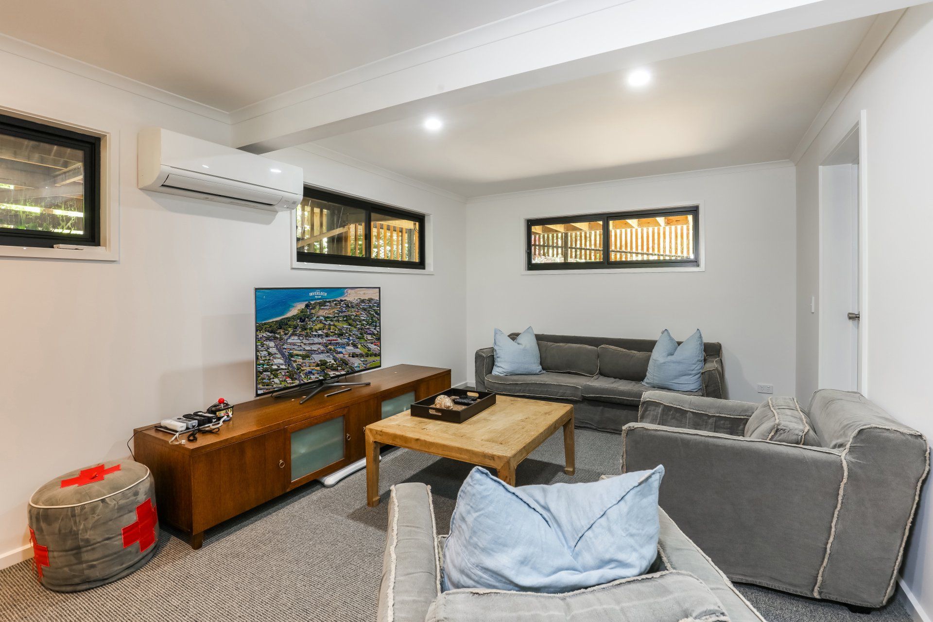 Modern living room with gray sectional, wooden coffee table, TV stand, and wall-mounted air conditioner
