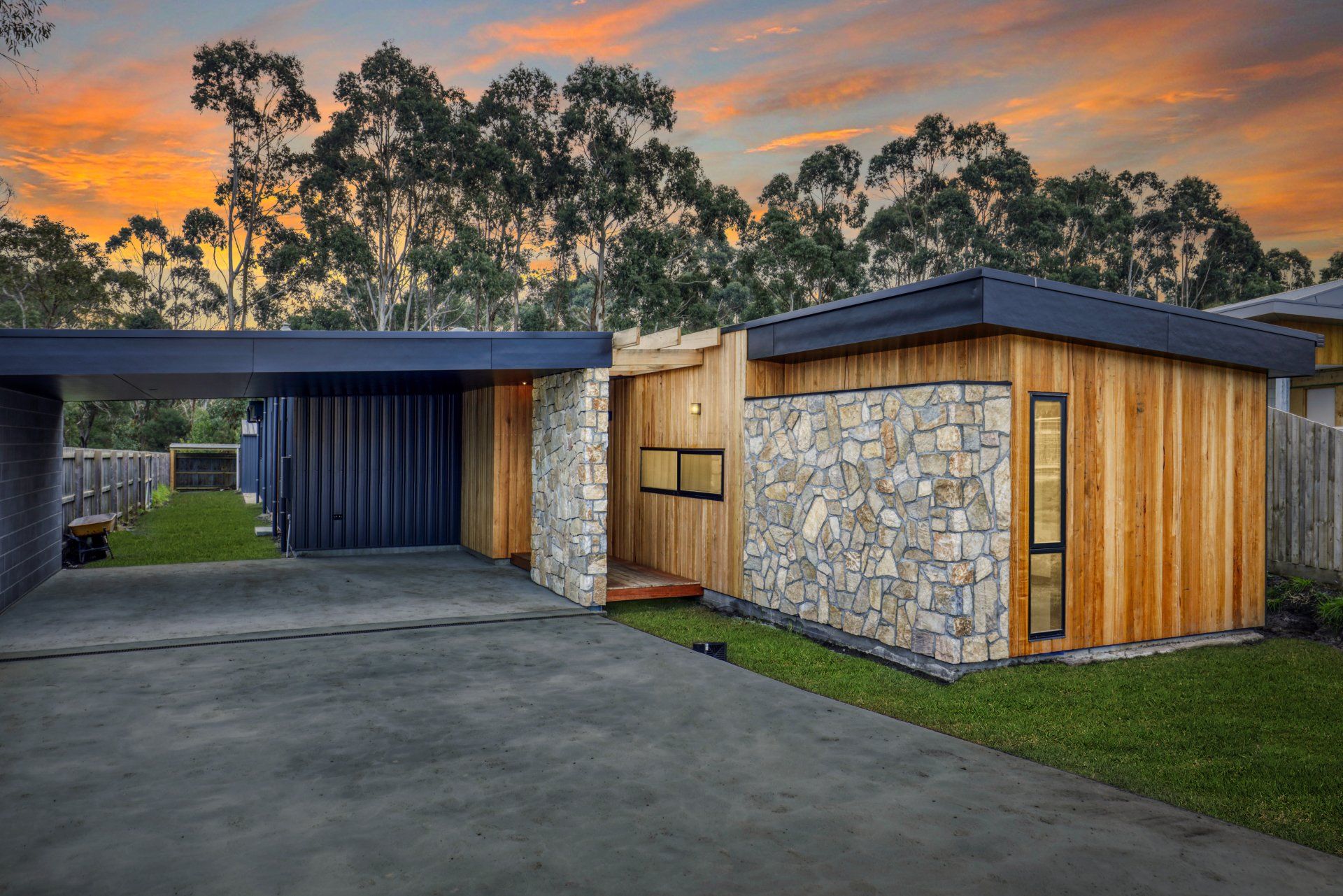 Modern house exterior with stone and wood siding, driveway, and carport at sunset