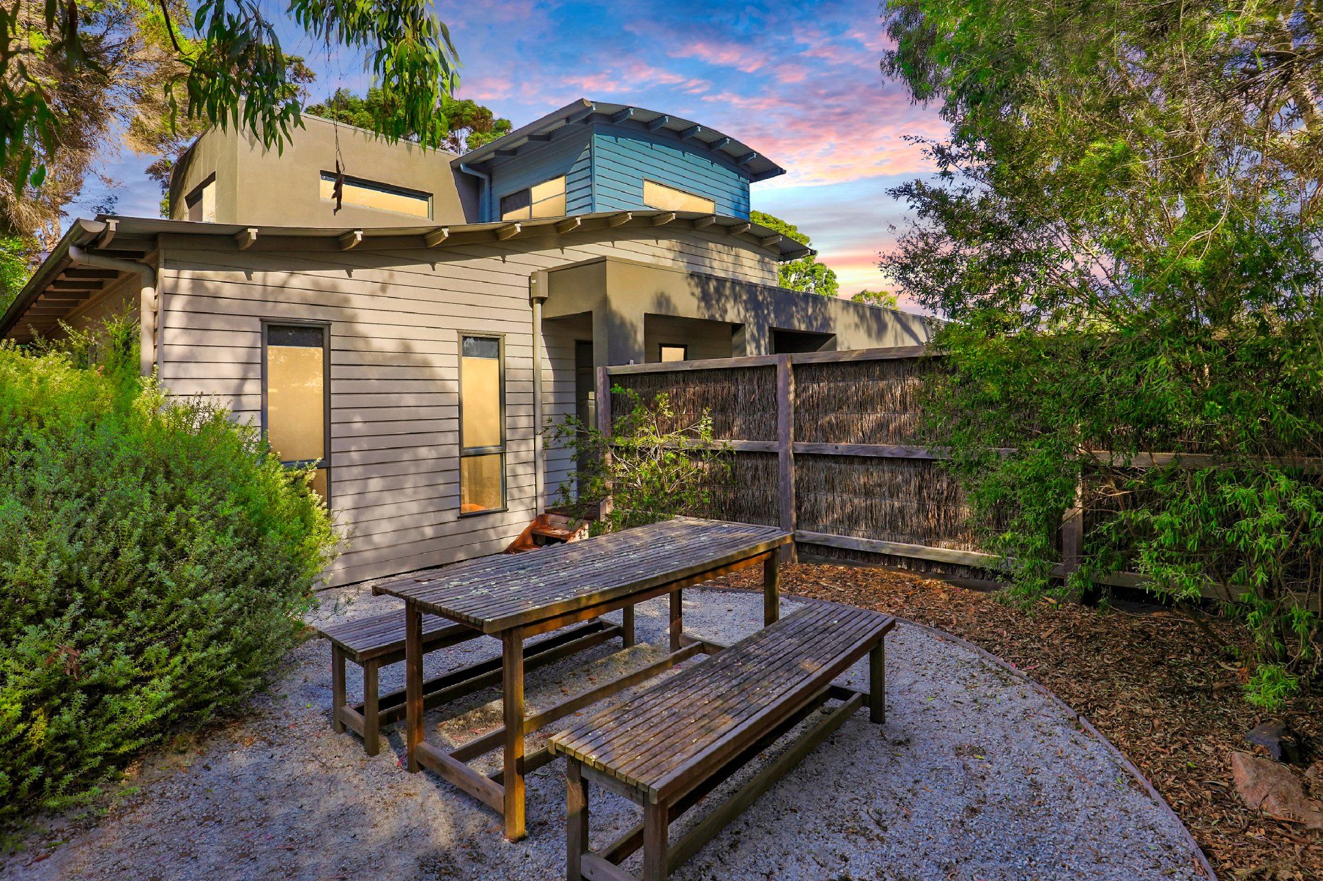 Outdoor patio with picnic table and benches beside a modern house at sunset