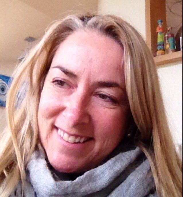 Smiling blonde woman in a gray scarf, close-up indoors