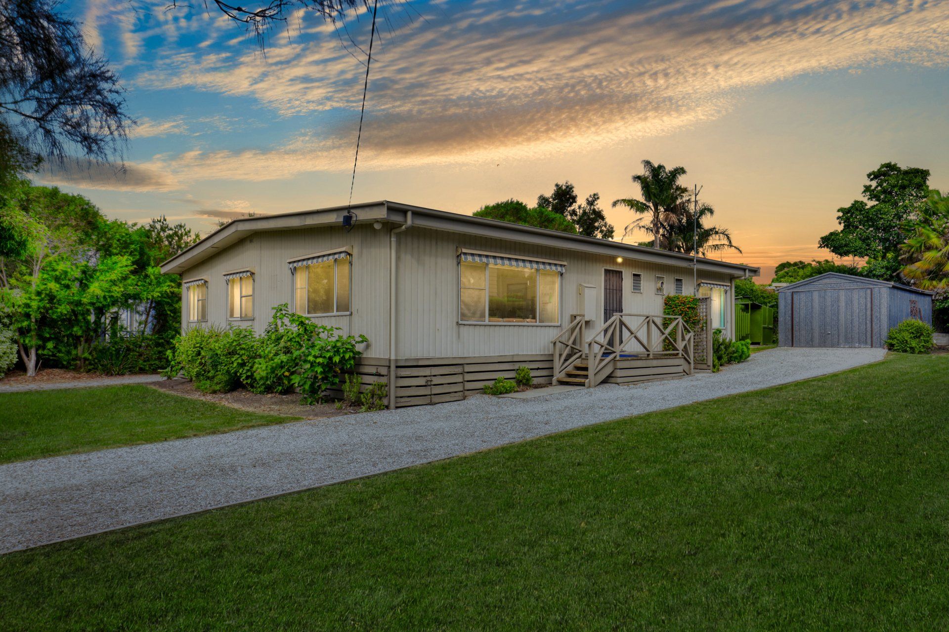 Single-story beige house with front yard and driveway at sunset under a colorful sky