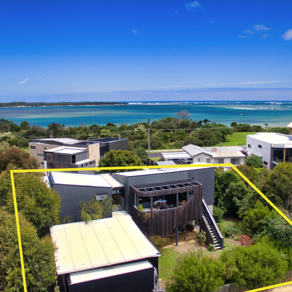 Coastal neighborhood with modern houses, lush greenery, and turquoise ocean under a clear blue sky