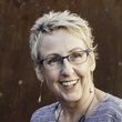 Smiling woman with short blond hair and glasses against a dark background