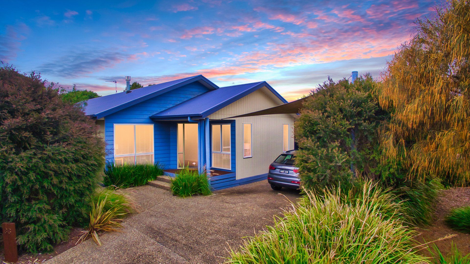 Modern house with blue trim at sunset, framed by trees and a parked car in the driveway
