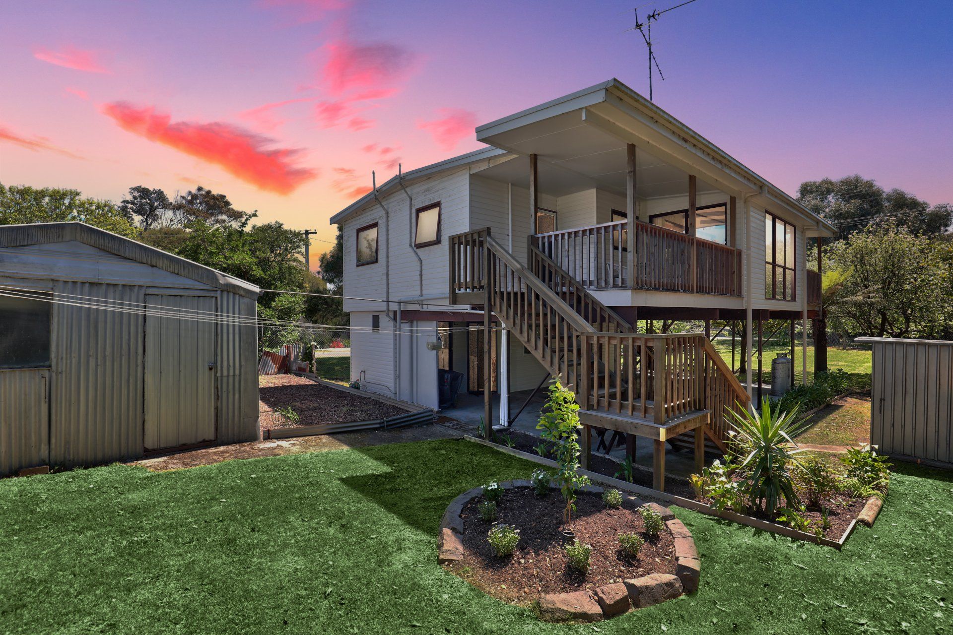 Backyard with a two-story house, wooden deck, and garden at sunset