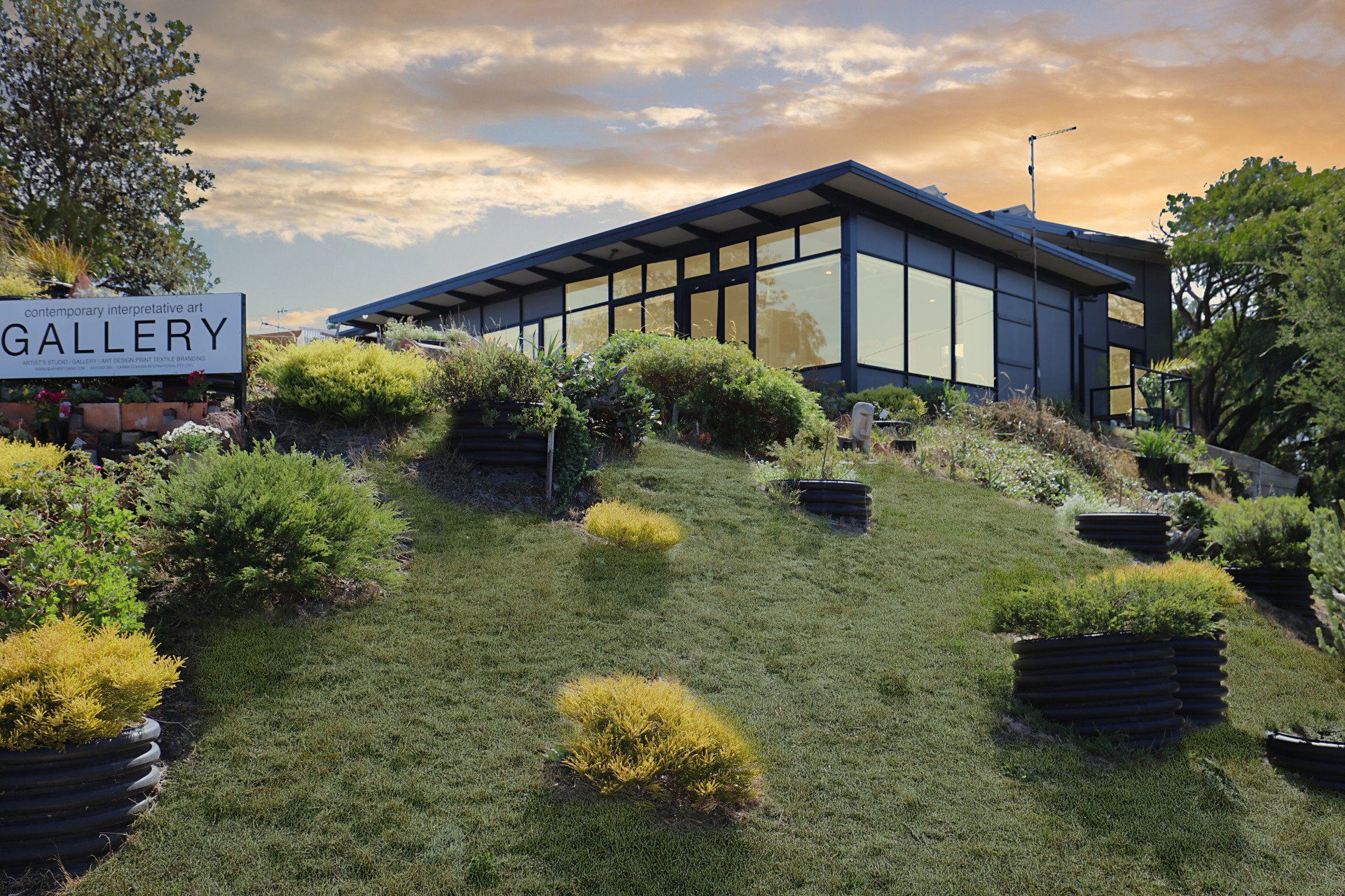Modern building on a grassy hillside with shrubs and a “GALLERY” sign at left