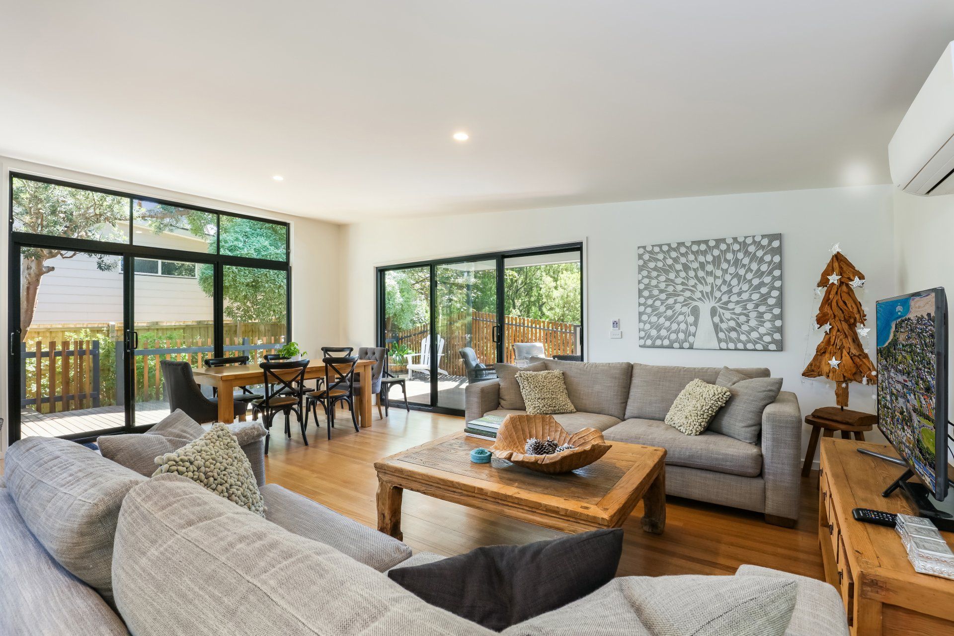 Bright living room with gray sofas, wooden coffee table, dining area, and large windows overlooking a balcony