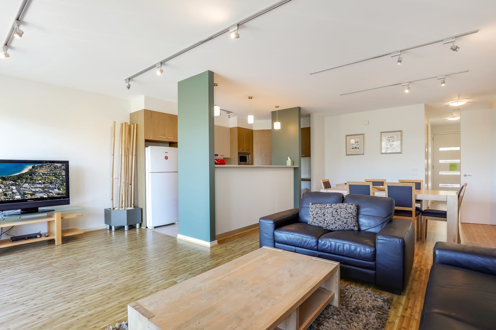 Bright modern living room with blue sofa, wooden coffee table, TV, and open kitchen area