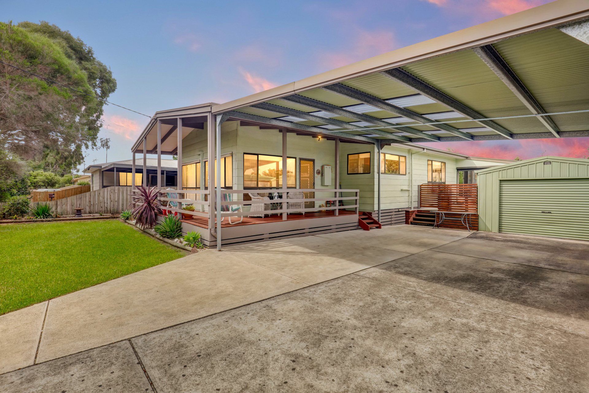 Suburban house exterior at dusk with a covered patio, driveway, and green lawn