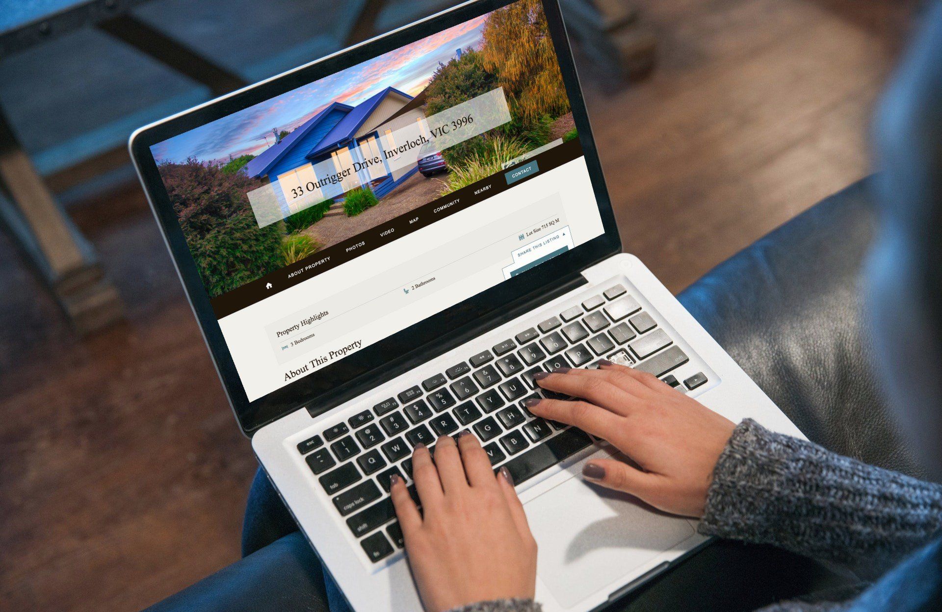 Hands typing on a laptop showing a website with a house photo on the screen.