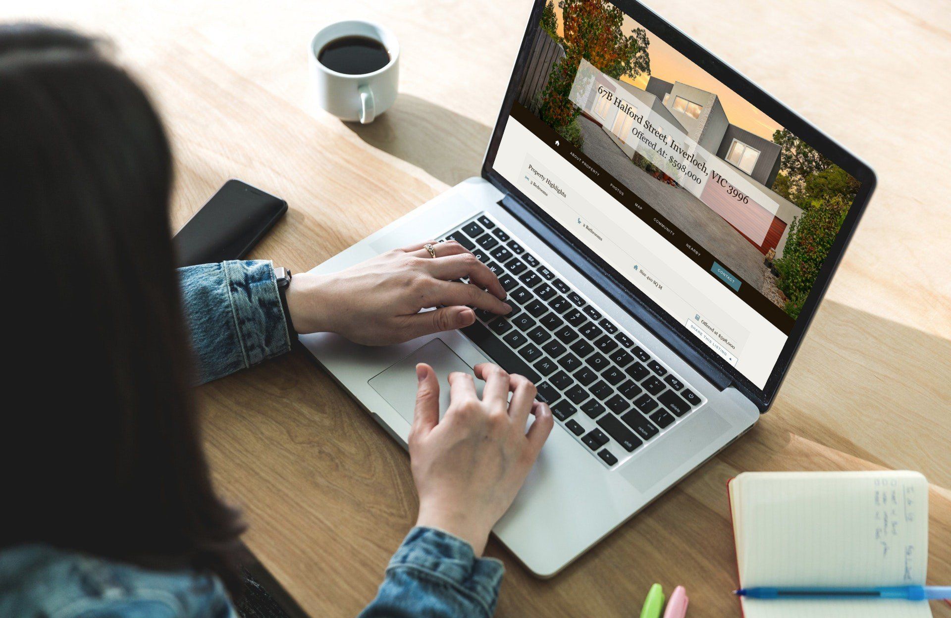 Person typing on a laptop at a wooden desk with a coffee mug and notebook nearby.