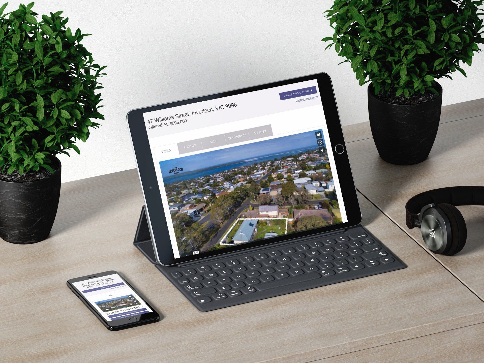 Tablet and phone on a desk with a video call on the tablet, flanked by two potted plants and headphones