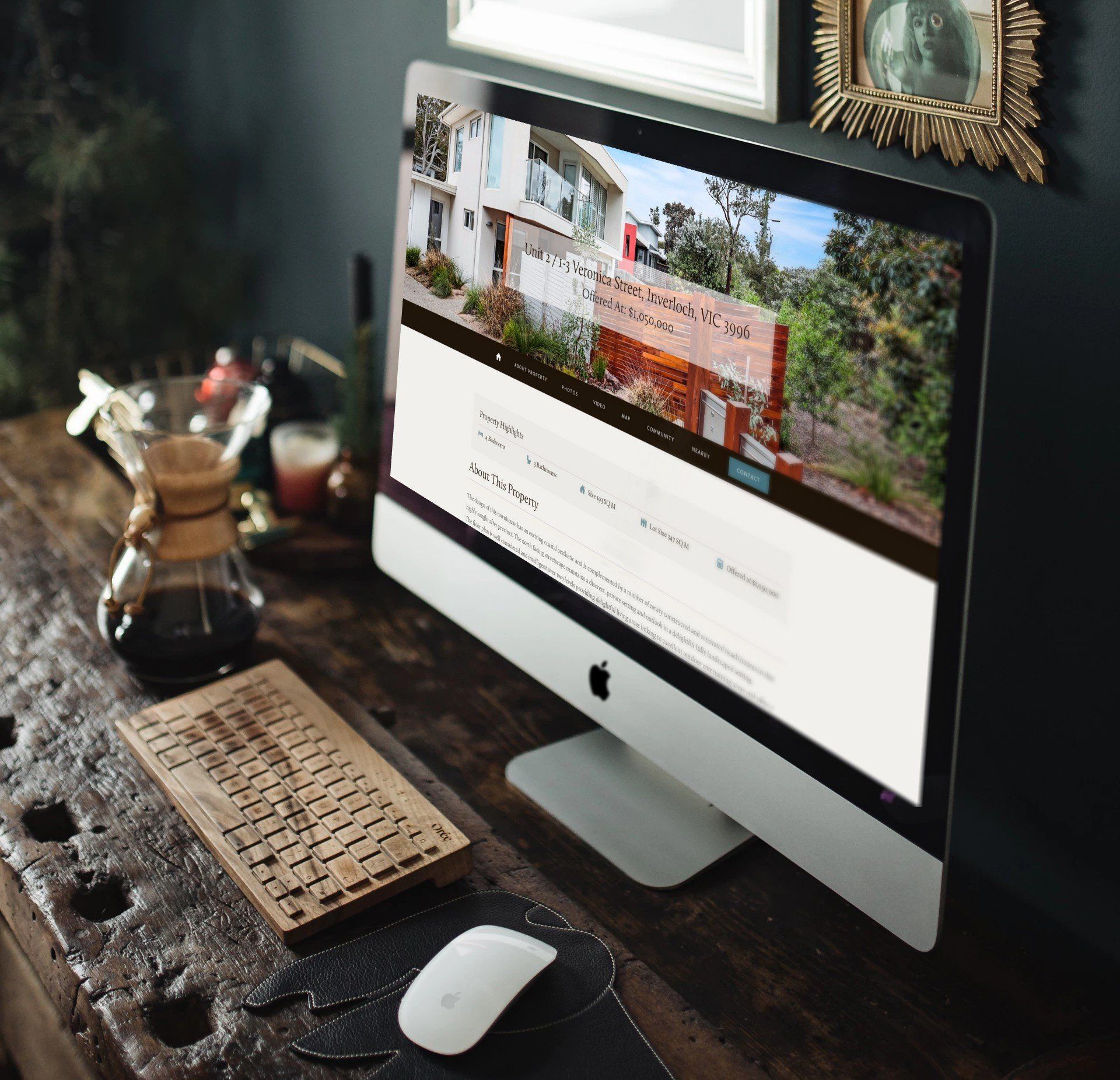 Desktop computer on a dark wooden desk with a keyboard, mouse, coffee pot, and framed wall art.