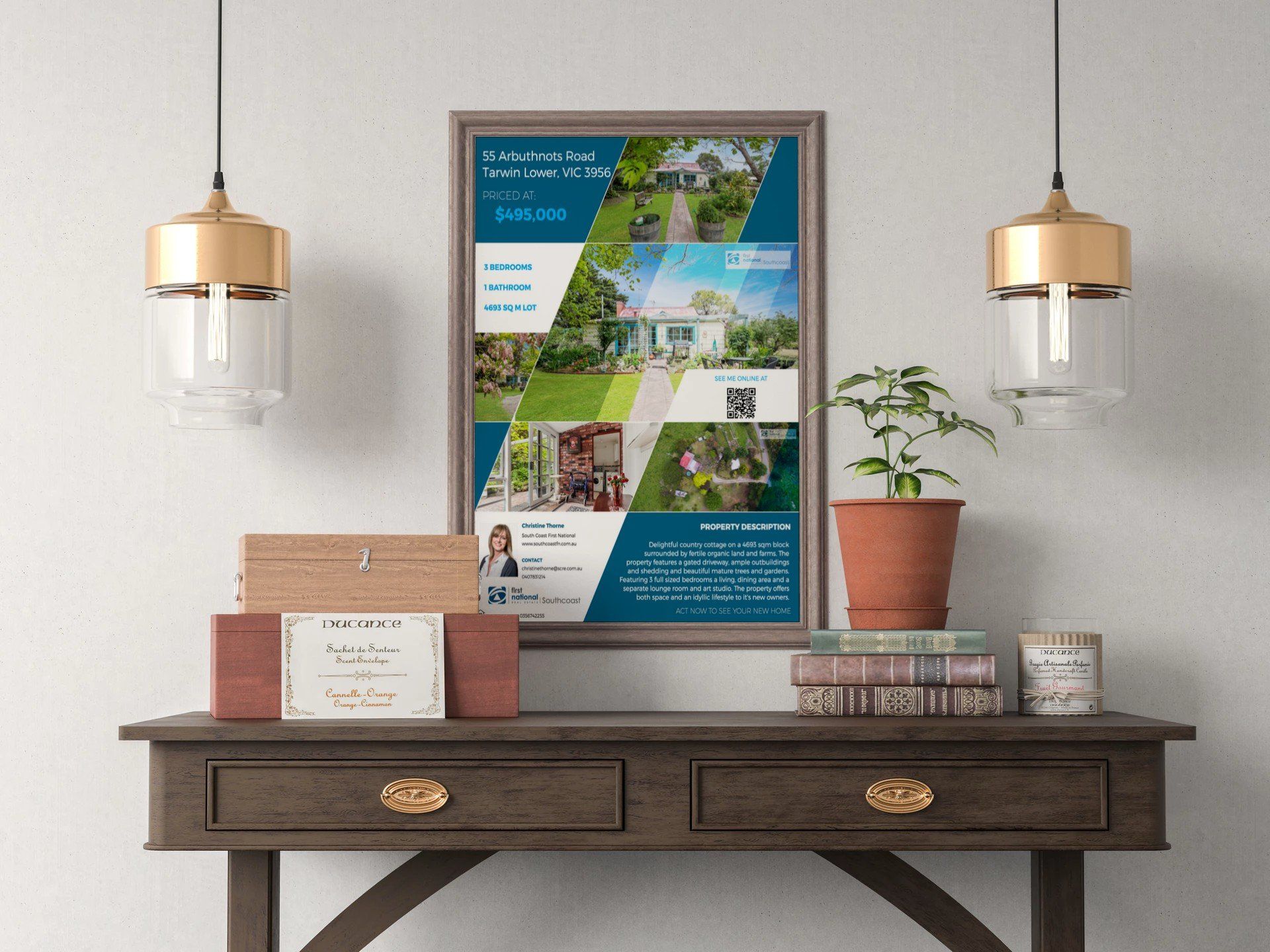 Framed travel poster above a dark wood console table with lamp, plant, books, and wall sconces