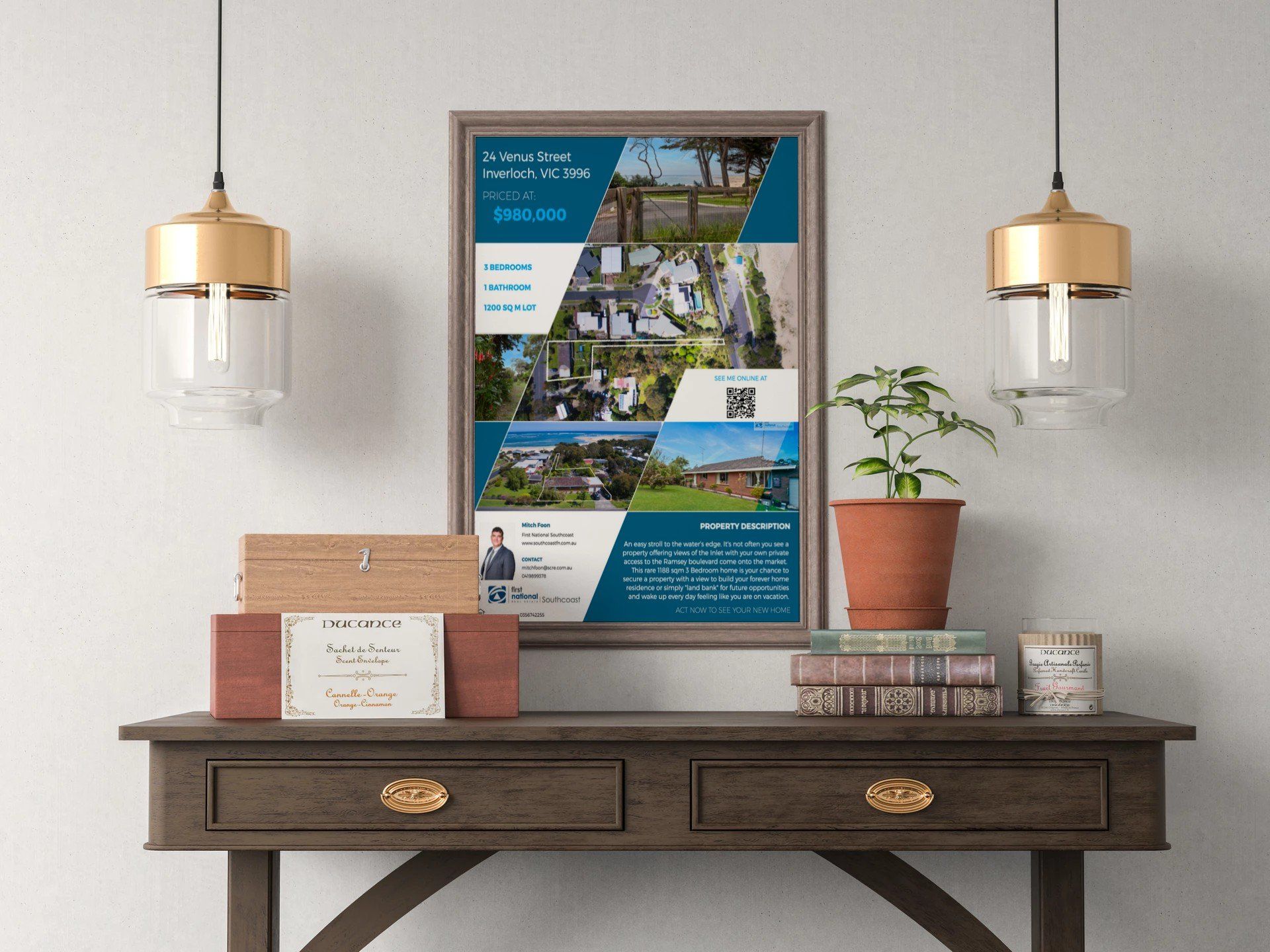 Framed poster above a dark wooden console table with books, plants, and hanging pendant lights