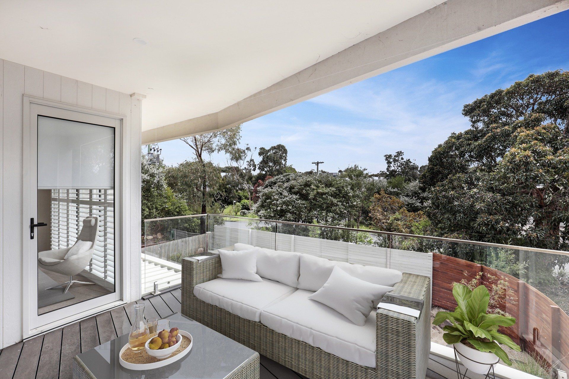 Modern balcony with white outdoor sofa, potted plants, and treetop view