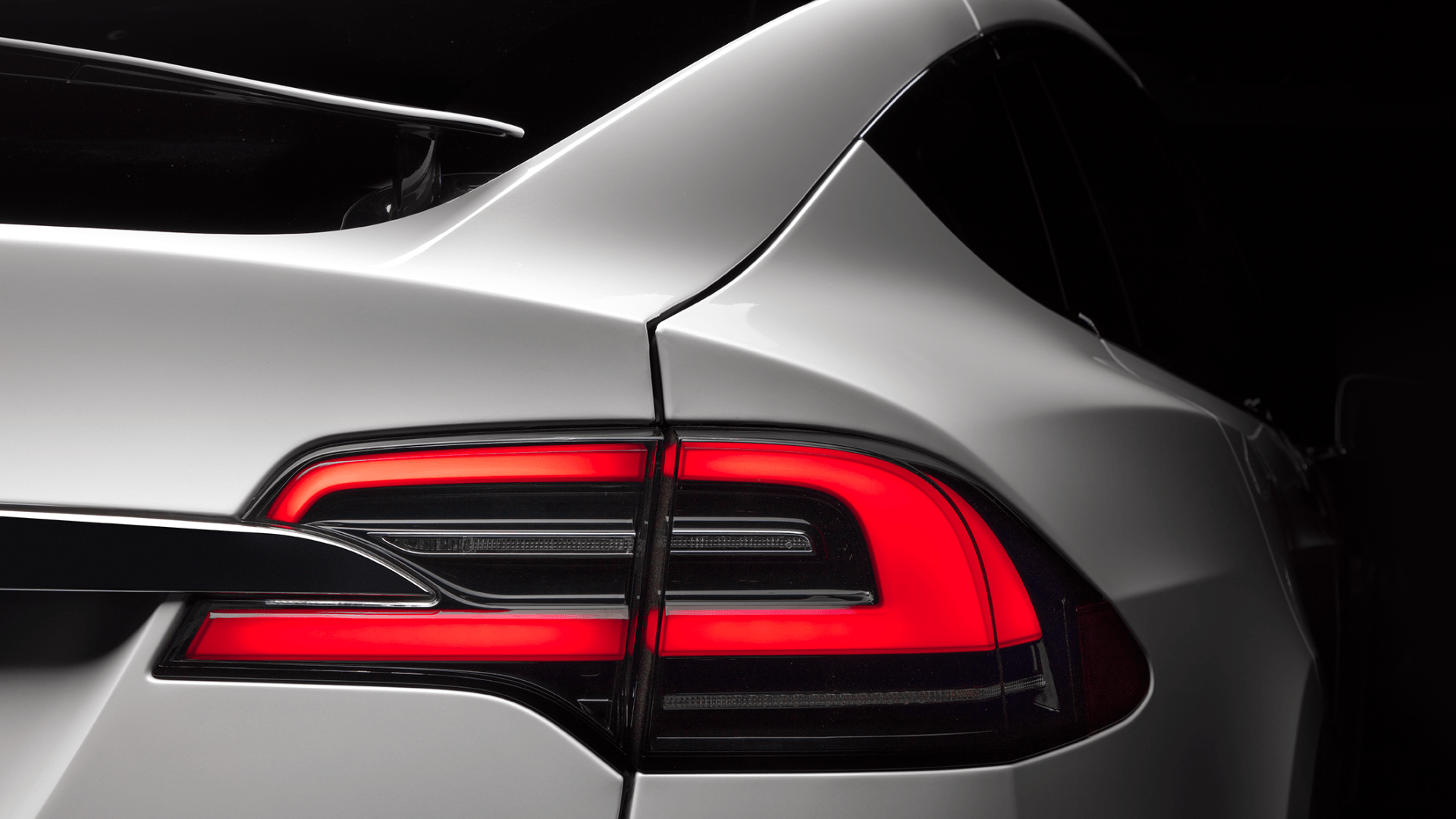 White Tesla Model X taillight illuminated red against a dark backdrop.