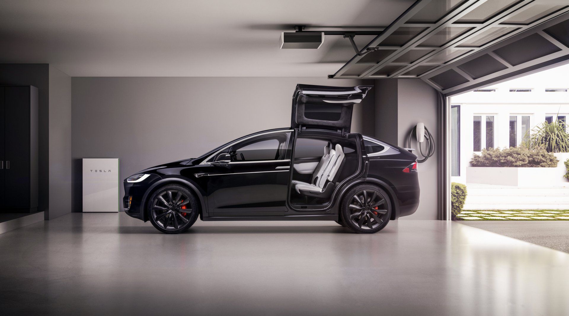 Black Tesla Model X with doors open in a modern garage, next to a white power unit.