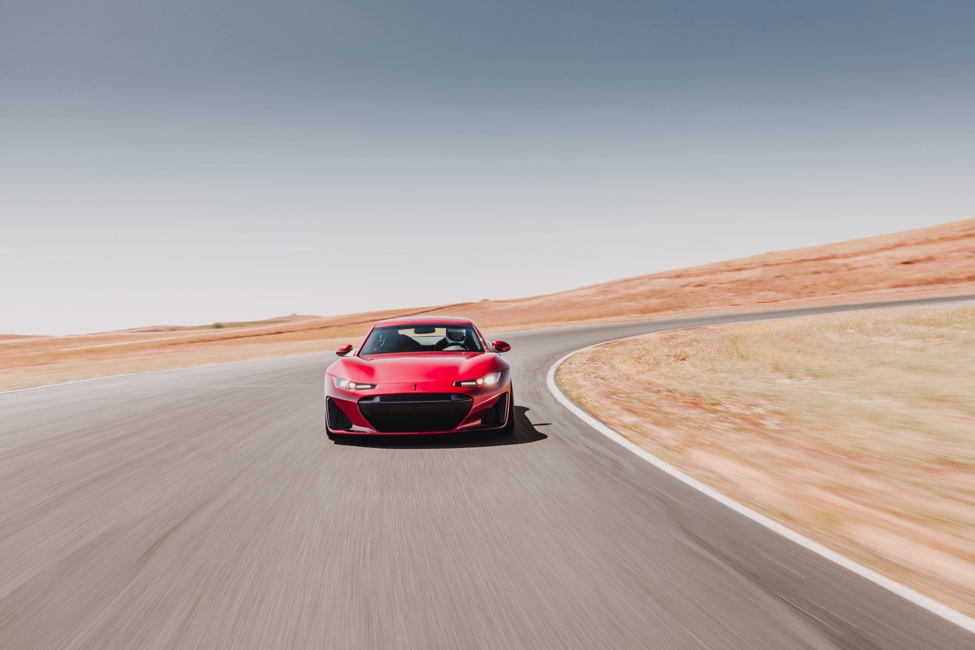 Red sports car driving on a racetrack, sunny day.