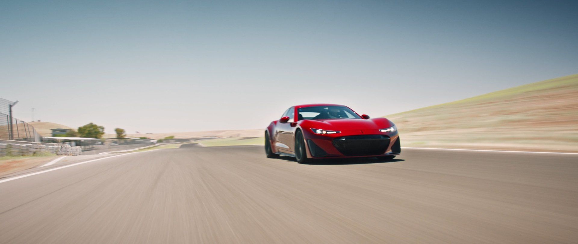 Red sports car speeding on a racetrack under a clear sky.