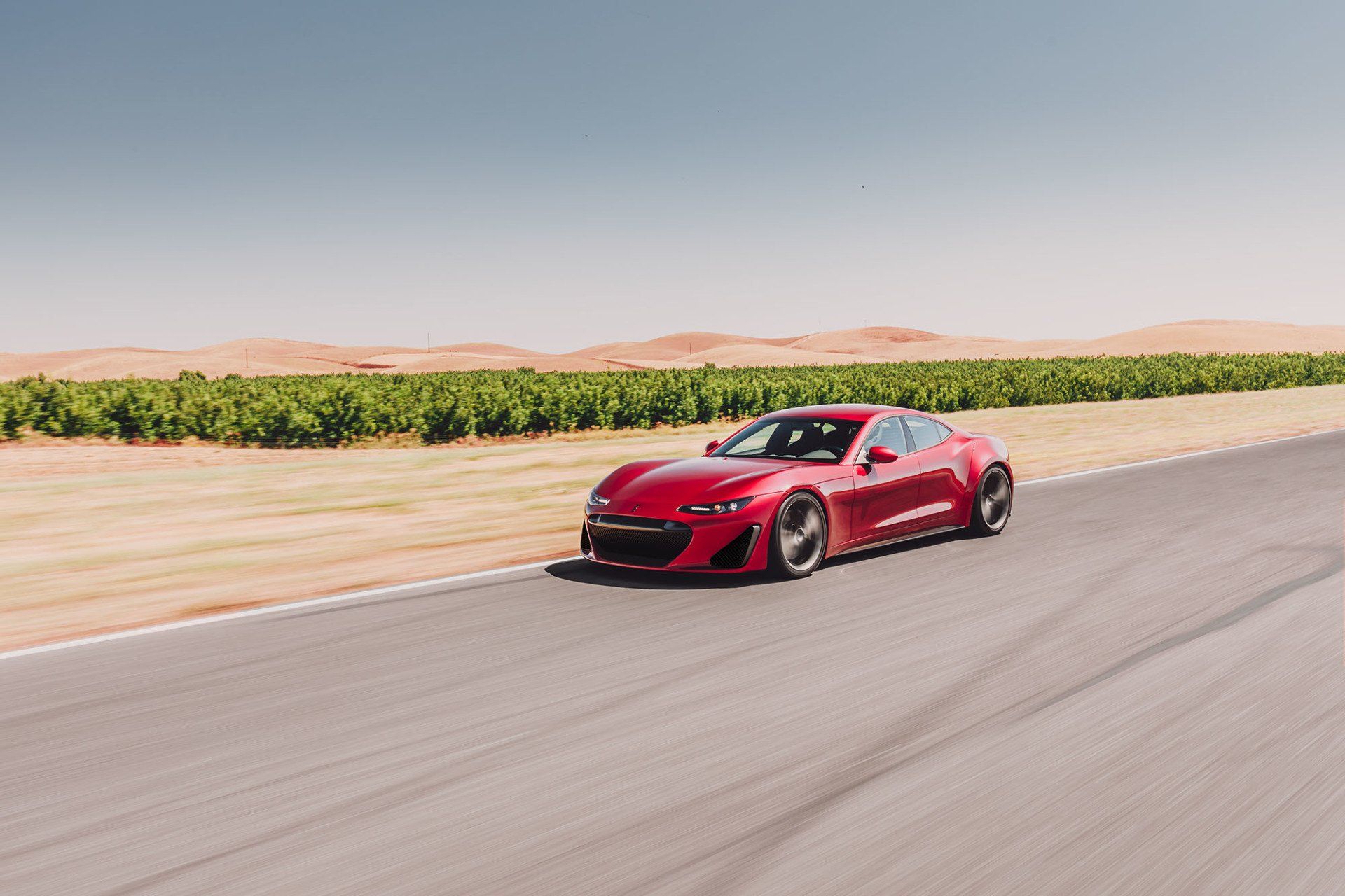 Red sports car on a race track, vineyards in the background under a blue sky.