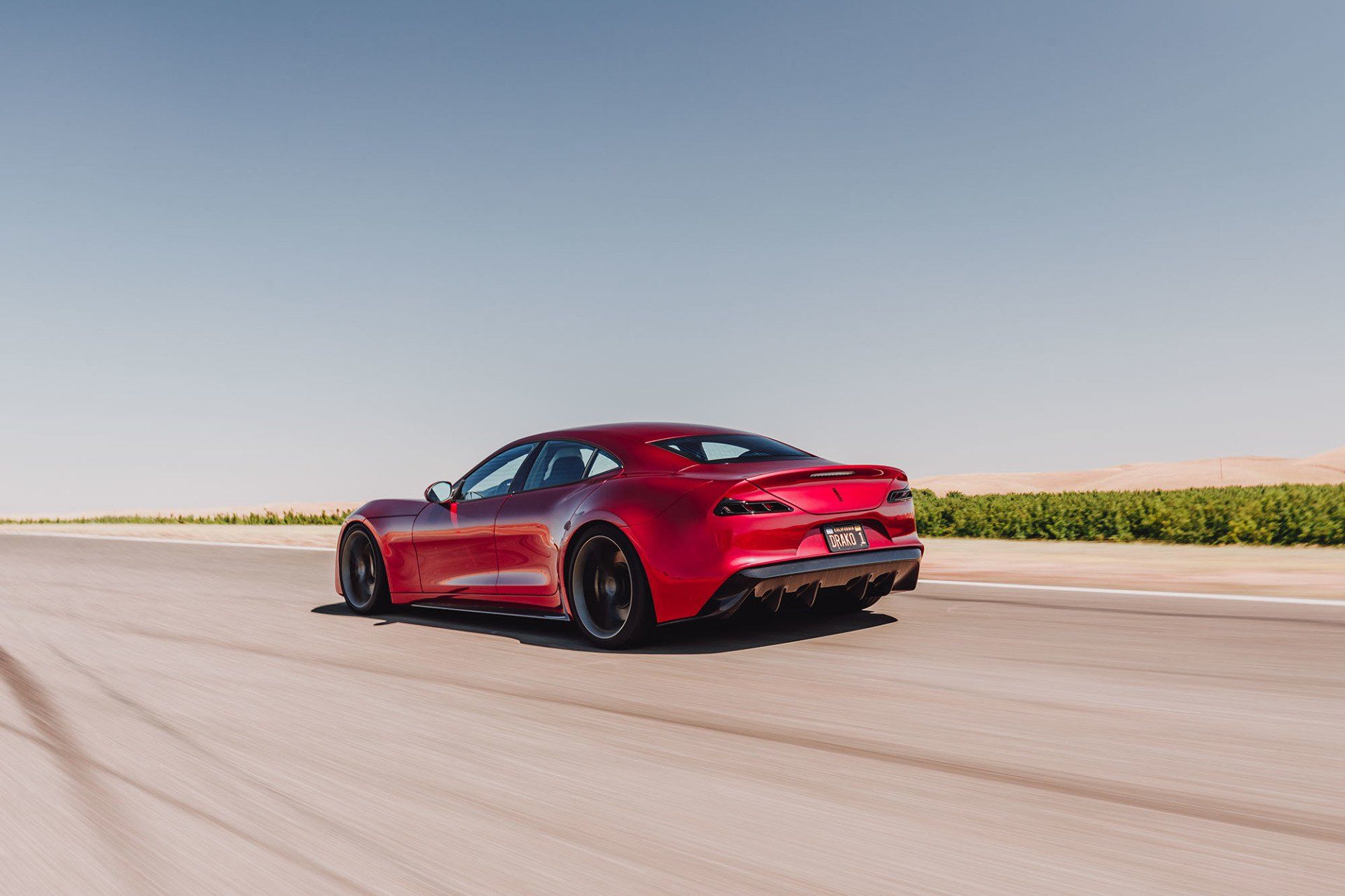 Red sports car driving on a road under a blue sky.