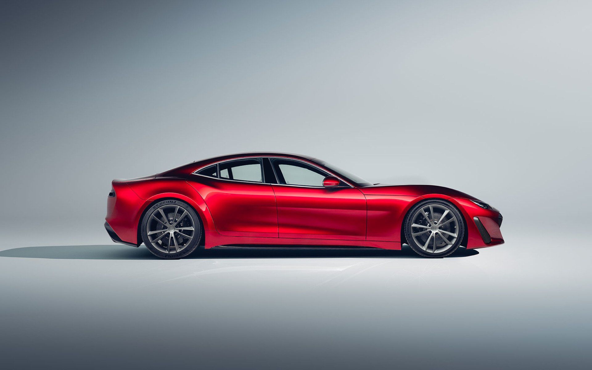 Red sports car parked on a light gray surface, side view.