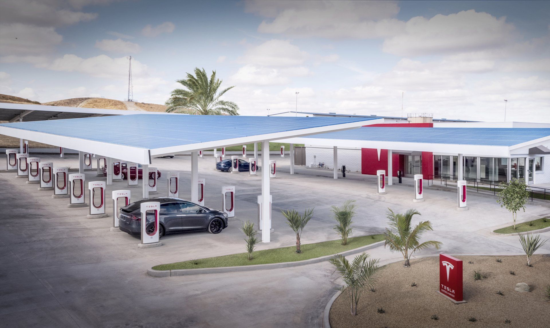 Tesla Supercharger station with solar panel canopy; cars charging.