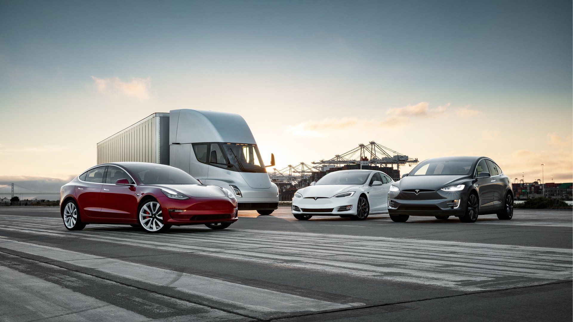 Tesla vehicles: red Model 3, white Model S, dark SUV, and Semi truck on a paved area.