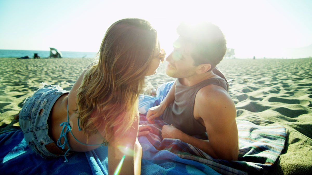 Couple kissing on a sunny beach, embracing. Blue bikini, ocean background.