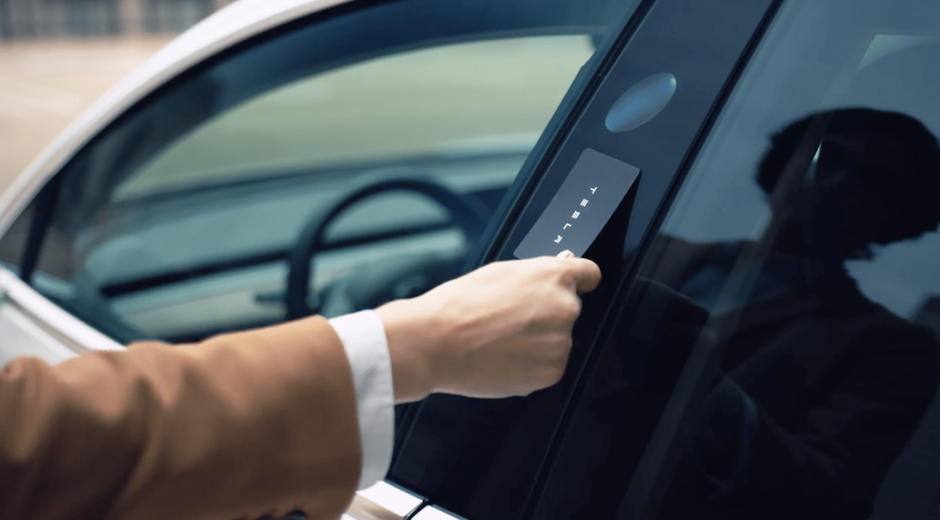 Hand holding a Tesla key card to unlock a car door.