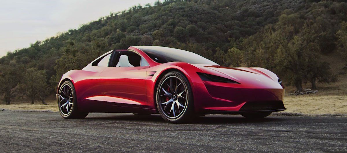 Red Tesla Roadster parked on an asphalt road in front of a hillside.