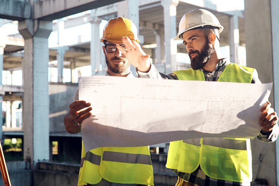 Dos trabajadores de la construcción con chalecos de seguridad y cascos revisan planos en un sitio de construcción.