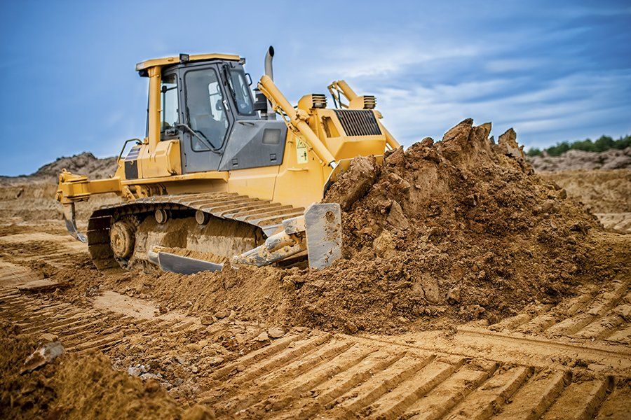 Una excavadora amarilla empujando tierra en un sitio de construcción bajo un cielo nublado.