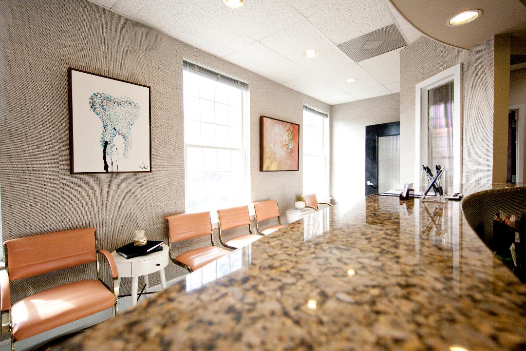 Modern office waiting area with orange chairs, framed art, and a glossy marble floor